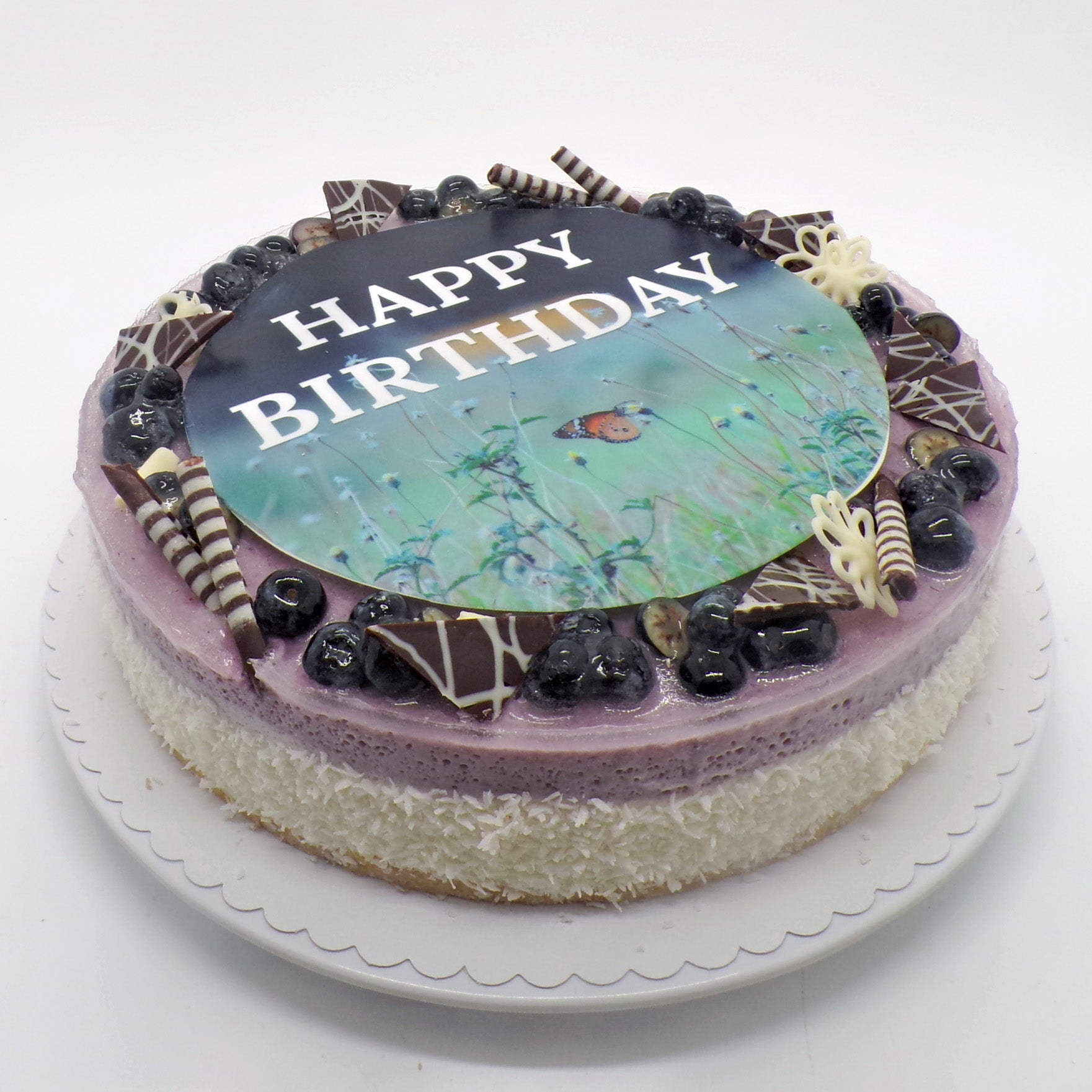 Blaubeertorte mit einem Zuckerbildaufleger auf dem ein Schmetterling auf einer Blumenwiese, darüber steht "Happy Birthday"